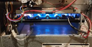 Inside of a furnace burn chamber, blue flames from natural gas burning and being directed down the main heat exchanger are visible.